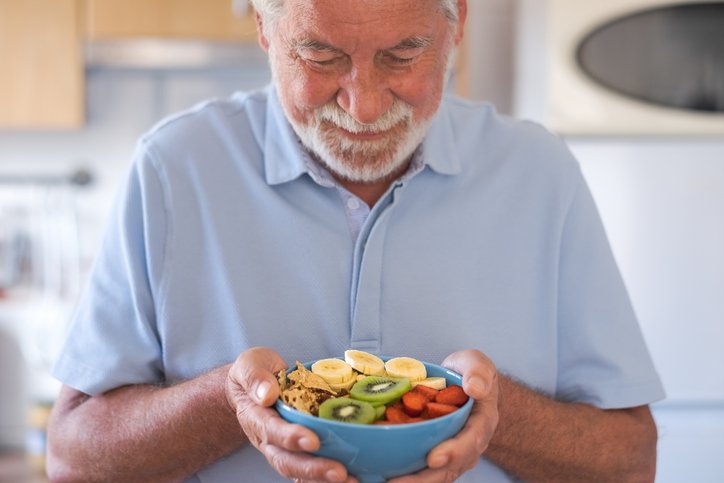 Smiling senior man ready to eat a salad of fresh and dried fruits. Breakfast or lunch time, healthy eating
